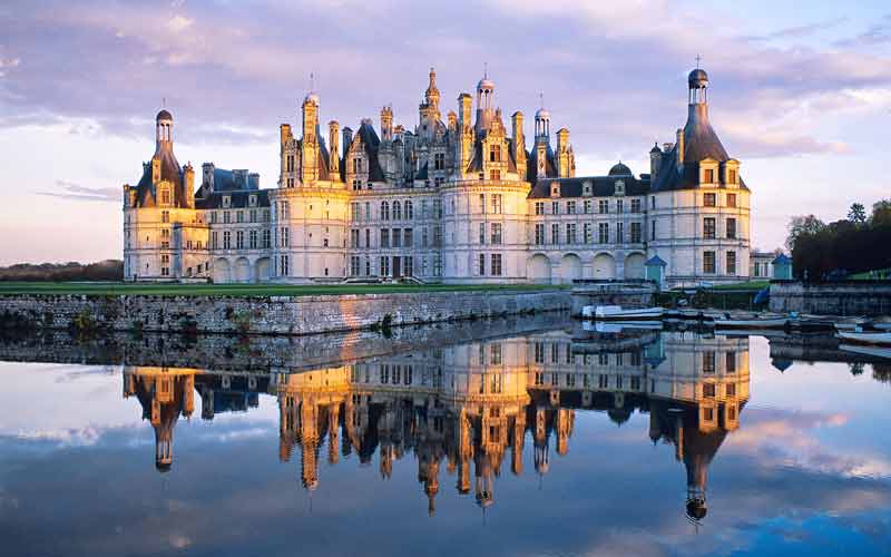 Château de Chambord au crépuscule, ciel rose reflété dans la rivière