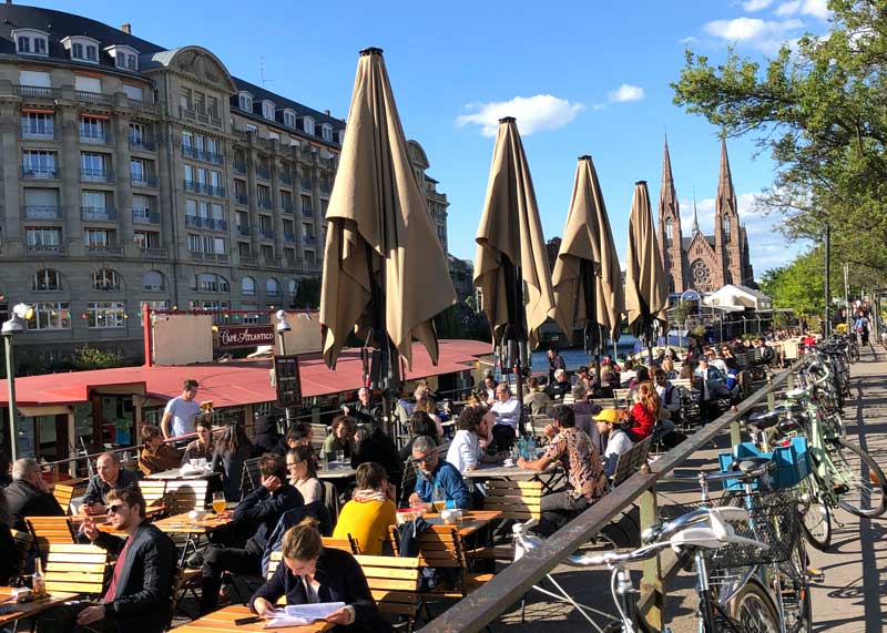 Beaucoup de gens assis au Quai des Pêcheurs prenant un verre au soleil à Strasbourg