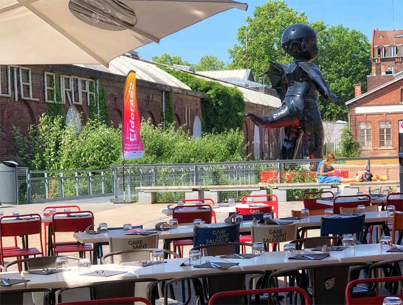 Bistrot de Saint So, Lille Tables et chaises sur une terrasse donnant sur une sculpture de bébé à queue géante à Lille