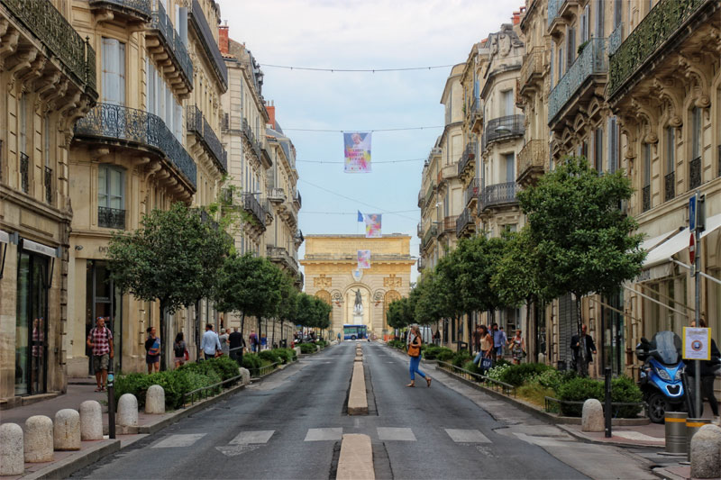 Promenade du Peyrou, Montpellier une longue rue bordée de hauts immeubles avec une arche au bout
