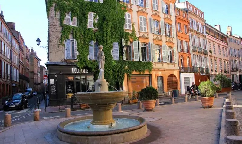 Jolie place bordée de bâtiments en briques rouges à Toulouse avec une fontaine au centre
