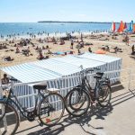 A long golden sandy beach under a blue sky, bikes leaning against railings