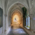 Very long cloisters of the Charterhouse of Neuville, sunlight casts a golden glow on the ancient paving