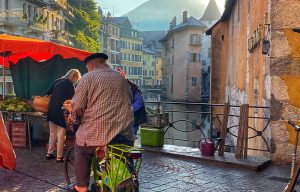 Man wearing a beret, riding a bike across a cobbled bridge in Annecy