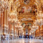 Gilded hallway of the Opera National in Paris, golden columns and plasterwork lit by chandeliers