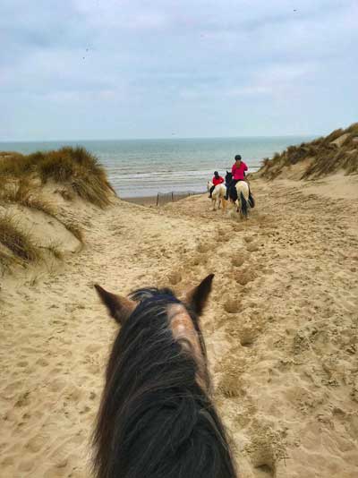 Des gens à cheval dans les dunes de sable menant à la mer au Touquet