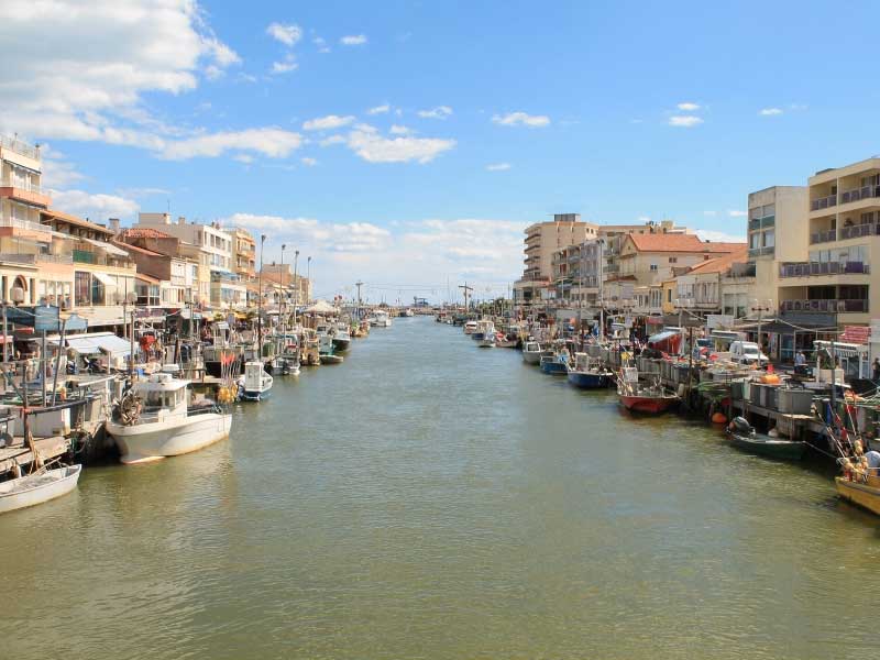 Une rivière mène à la mer à Palavas-les-Flots, dans le sud de la France, des cafés bordent les quais, des bateaux flottent dans l'eau