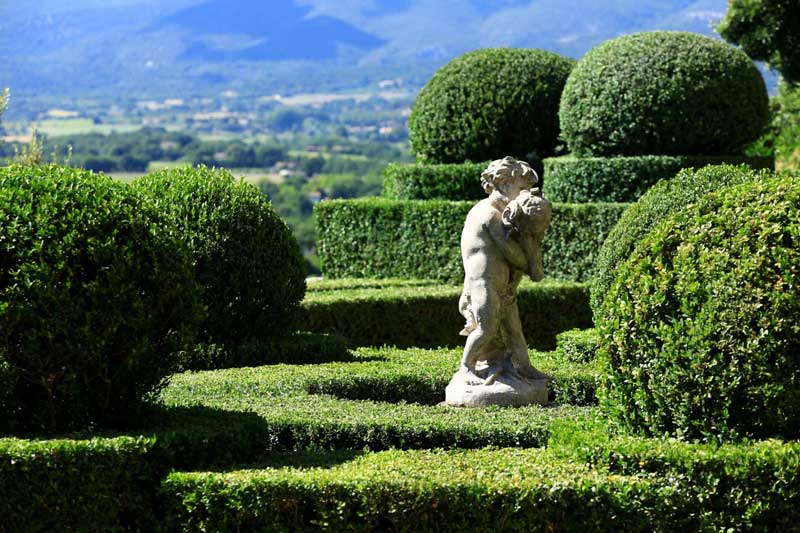 Ansouis, Luberon Photo : Office de Tourisme Luberon Côté Sud Statue en pierre blanche dans une mer de topiaires verts dans un jardin à Ansouis, Provence