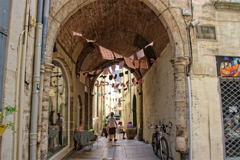 Rue de la Friperie, vieille ville de Montpellier, idéale pour une balade ombragée au soleil d'été Des banderoles à rayures roses et blanches sont suspendues sur une passerelle voûtée bordée de bâtiments anciens à Montpellier