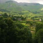 High hills covered with grass and trees surround a tiny village in a valley