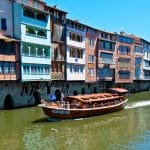 A boat cruising along a river lined with houses in Castres, France