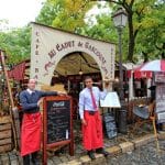 Two waiters with red aprons tempt passers by to a pretty restaurant in Montmartre Paris