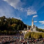 A huge square filled with people at Lourdes in France with church spires in the background
