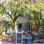 Pretty cafe in a village in Provence, leafy terrace with tables outside on the terrace
